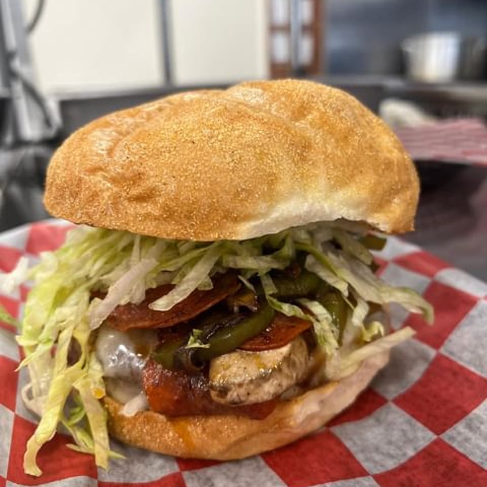 Chief's Steak Shop sandwich with pepperoni, green peppers, cheese, and shredded lettuce on a bun.