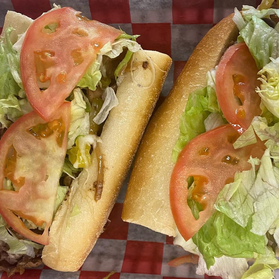 Two Chief's Steak Shop sandwiches with steak, lettuce, and tomato on a red and white checkered paper.