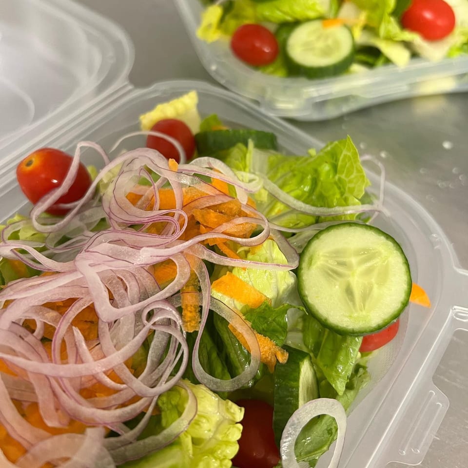 Fresh side salad with lettuce, tomatoes, cucumbers, shredded carrots, and red onion in a plastic container.