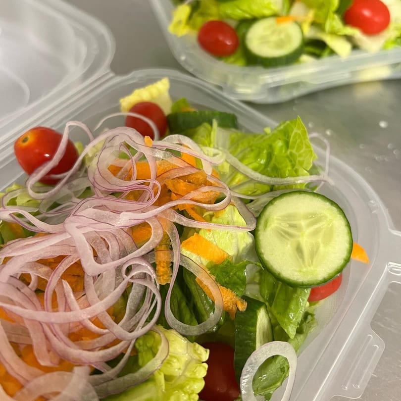 Fresh side salad with lettuce, tomatoes, cucumbers, shredded carrots, and red onion in a plastic container.